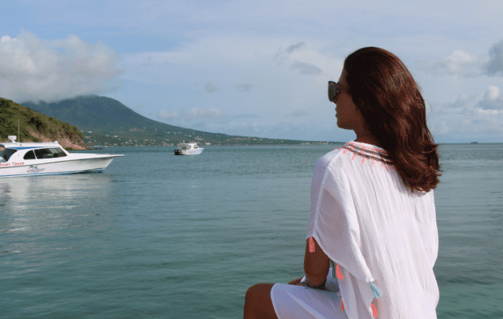 A woman sitting on a boat and gazing across the water at another boat in the distance, while wearing a pair of sunglasses.