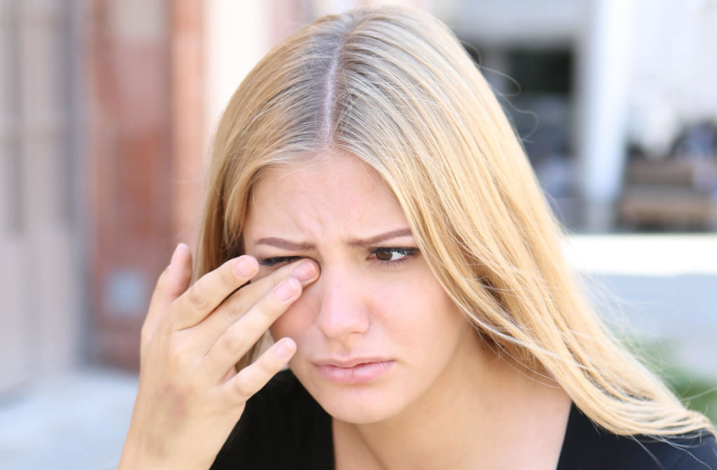 A woman is touching and rubbing her right eye with a gesture of irritation on her face.