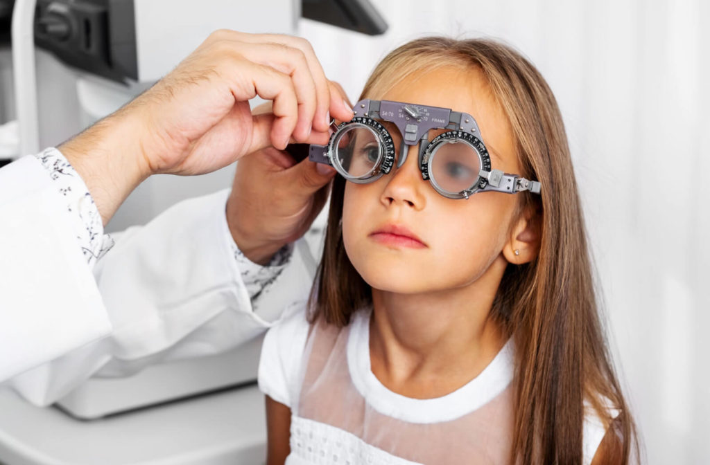 A young girl is wearing a phoropter while the optician is changing the lens to manually determine the “refraction” of the eye.