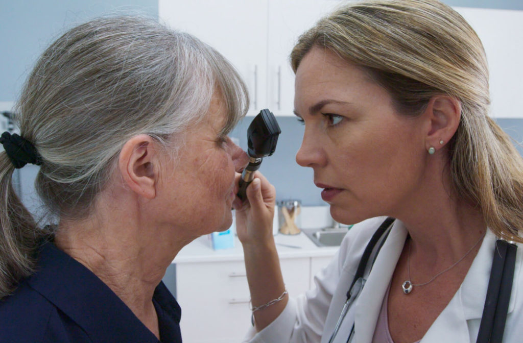 A close-up of a female doctor using an ophthalmoscope to look into older patients eyes