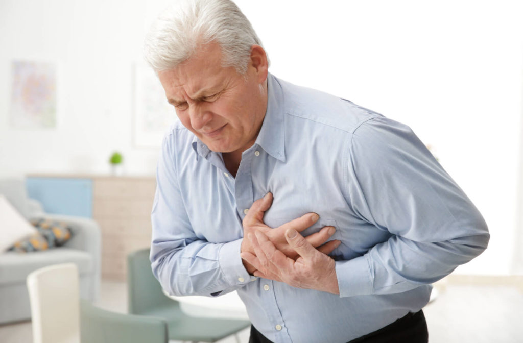 A senior man holding his chest due to chest pain suffering from a heart attack. Signs of heart disease can be detected during eye exams.