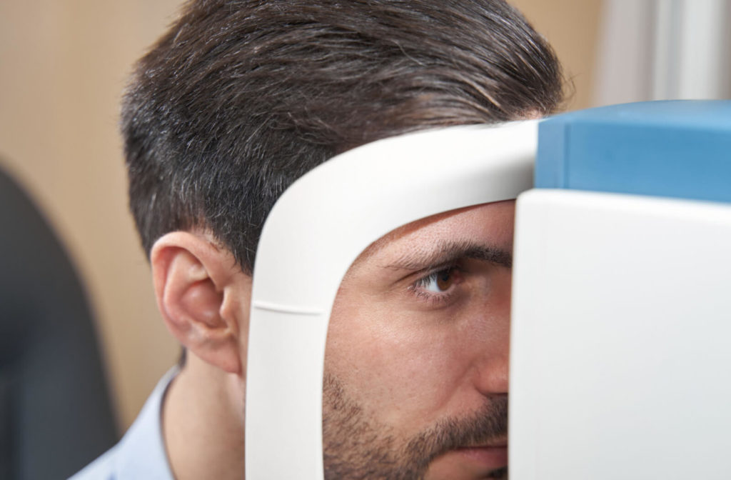 An adult male is sitting in front of an autorefractor and his chin resting on a chin rest while looking through the machine.