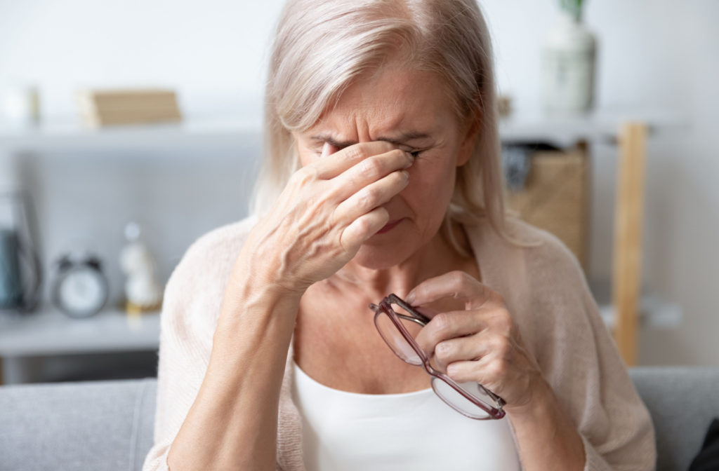 A senior woman rubbing her eyes with her hand while holding her eyeglasses with left hand.