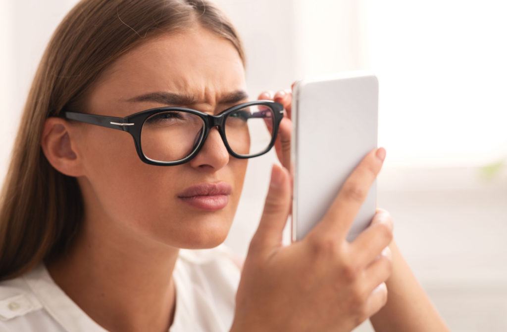 A woman adjusting her glasses and squinting at her phone screen.