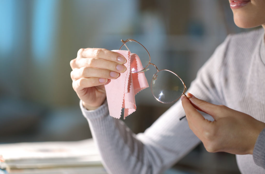 A woman cleaning a pair of eyeglasses using a pink microfibre cloth.