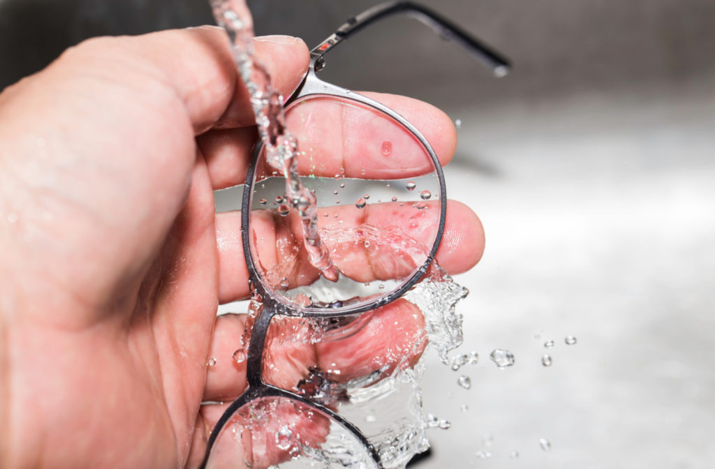 A close-up of a hand rinsing a pair of eyeglasses using running water.