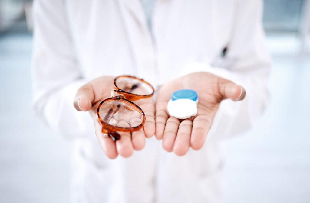 An optometrist holding up a pair of corrective eyeglasses and a plastic container of a contact lens.