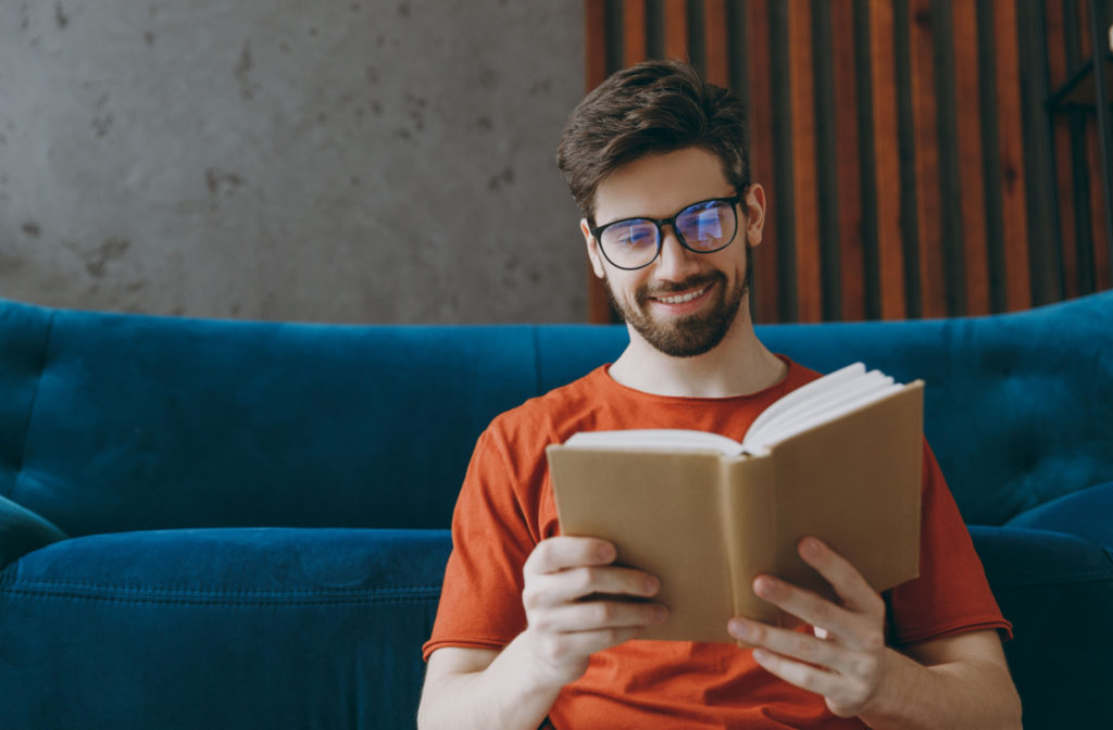 A man wearing reading glasses happily reading a book.