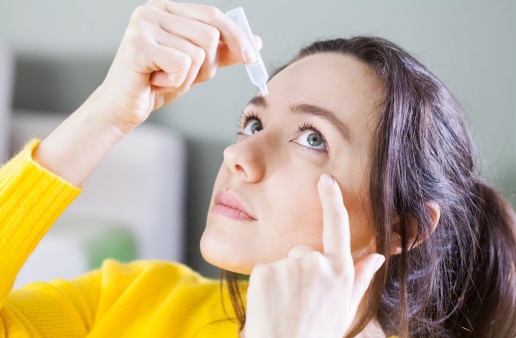 A woman pulling her left lower eyelid to apply eye drops.