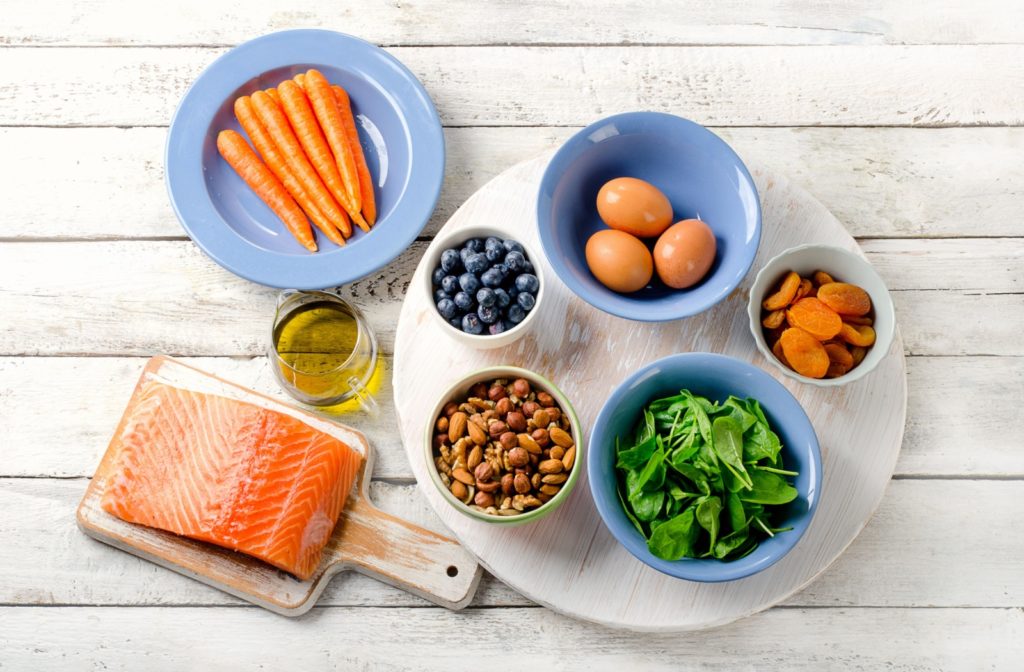 An assortment of food that can improve and maintain eye health, including salmon, carrot, fruits, and more.