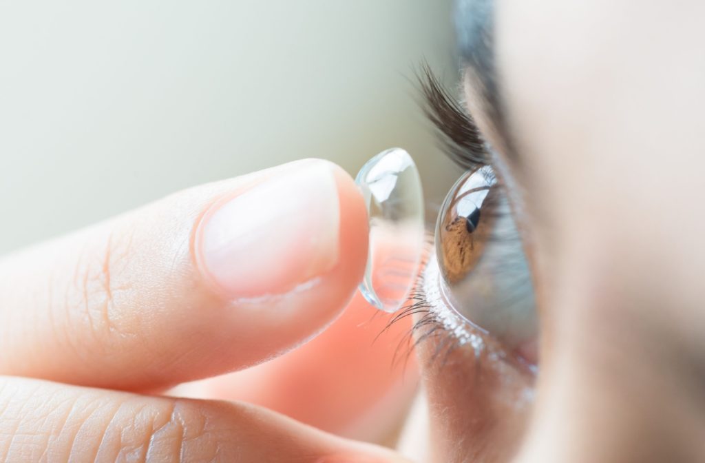A close-up of a woman with brown eyes is in the process of inserting her contact lens.