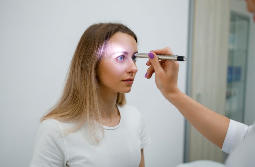 An eye doctor checks pupillary response by passing a light over a lady's eye.