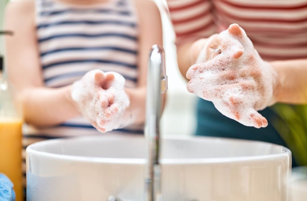 A young child and parent thoroughly wash their hands together.