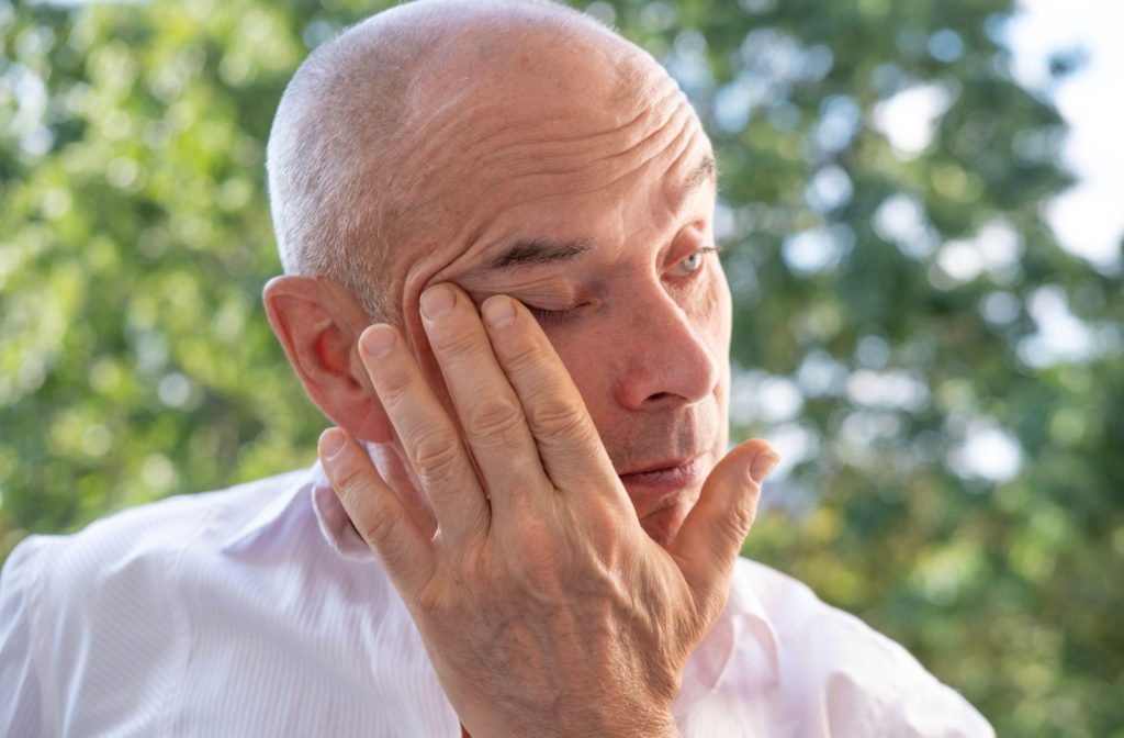 An older adult rubbing their right eye from grittiness and dry eye.