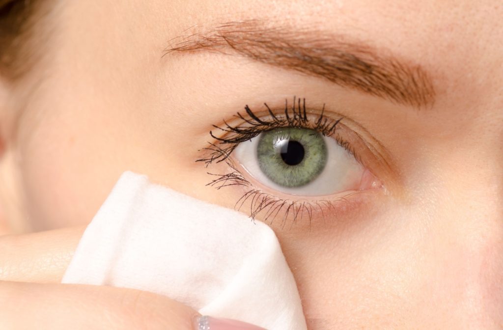 A close-up image of a person cleaning their eyelids with a lid cleansing wipe.