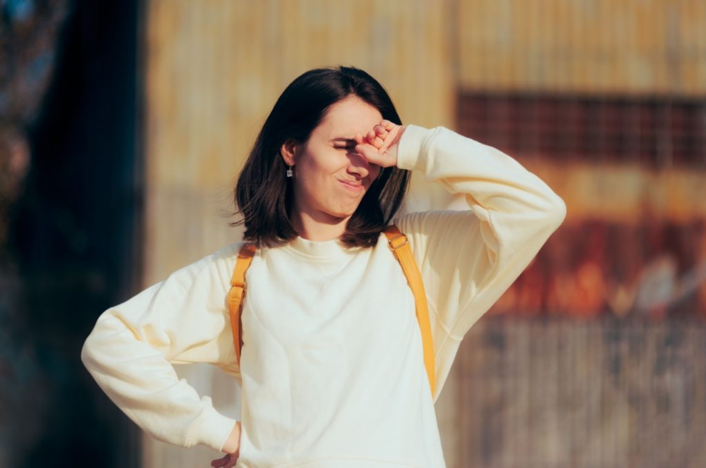 A woman with eyes closed and their hand blocking the sunlight from light sensitivity.