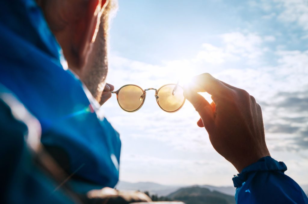 A behind image of a person putting on sunglasses while outside on a sunny day.