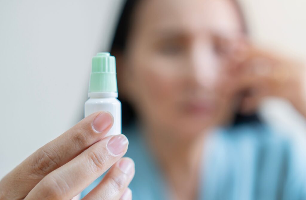 Person holding a bottle of eye drops with blurred background.