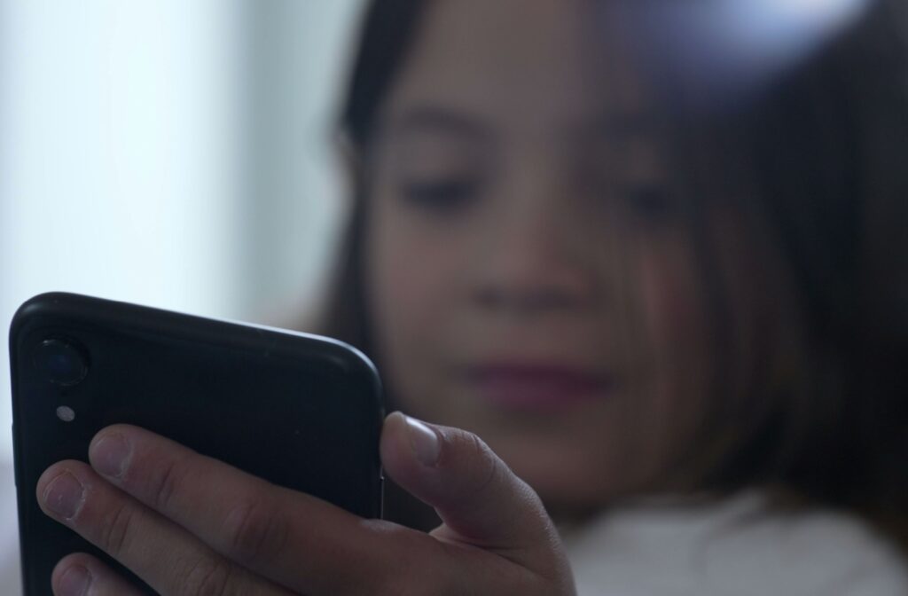 A child looking at a phone screen close up, contributing to the cause of nearsightedness.